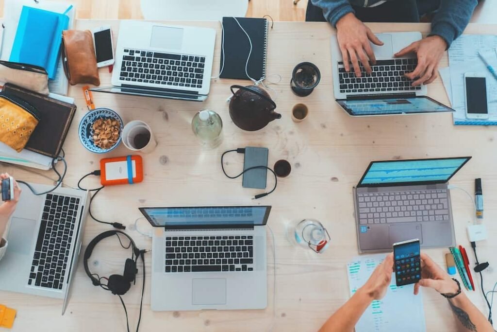 A busy table full of people using their laptops, headsets, and phones.